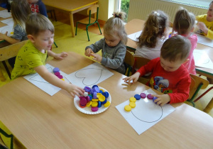 Dzieci układają nakrętki plastikowe na szablonie figur geometrycznych.